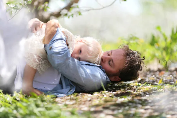 一个快乐的父亲正在亲吻他两岁的小女儿 因为他们躺在外面开花的苹果树下 在一个春日 — 图库照片