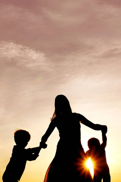 Silueta de Madre Feliz y Pequeños Niños Bailando Fuera de un —  Fotos de Stock