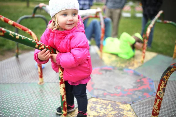 Pequeña niña jugando en Merry-Go-Round en el parque infantil —  Fotos de Stock