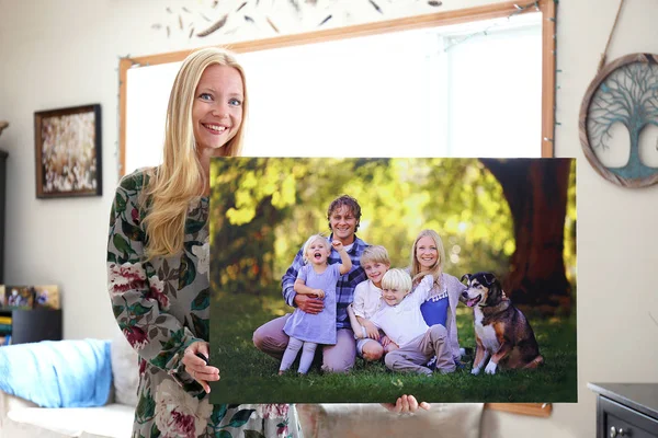 一个快乐的年轻金发女郎拿着一个大墙帆布肖像她的家庭与年幼的孩子和一只宠物狗 — 图库照片