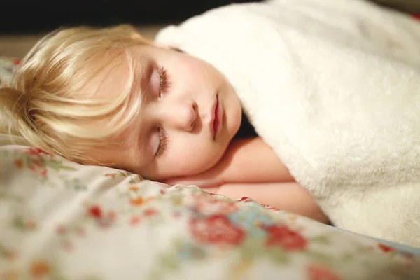 A beautiful two year old toddler child is sleeping peacefully on a floral pillow and white fluffy blanket.