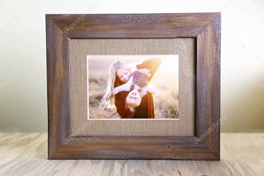 A tabletop display of a rustic wood framed print holding a portrait of a happy young mother holding her baby daughter outside at suset.