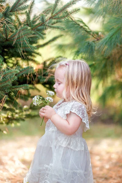 园中的花香芬芳中，穿着白色花边衣服的蹒跚女孩 — 图库照片