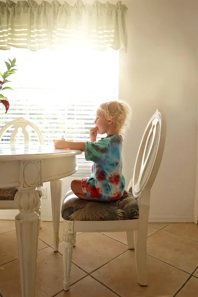 かわいい小さな幼児の女の子は彼女の家族の夕食のテーブルに座っています晴れた朝に 窓のそばで朝食のシリアルを食べます — ストック写真