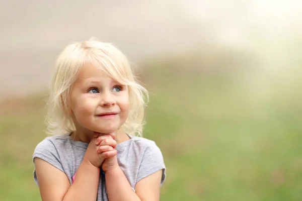 彼女は彼女の手を折ると夏の日に外で祈るように美しい小さなクリスチャンブロンドの髪4歳の女の子子供は甘い笑顔です — ストック写真