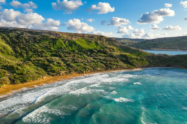 Ghajn Tuffieha sahilinin havadan görüntüsü. Gün batımı, mavi gökyüzü, yeşil dağ, denizde dalgalar. Kış. Malta