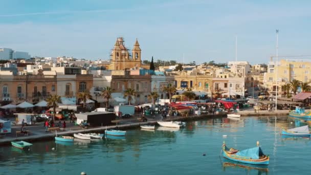 漁村Marsaxlookの空中ビュー 主教会 海岸線 カメラの前を飛んで鳥の伝統的なマルチボート カメラは右側に移動します マルタ国 — ストック動画