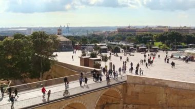 Malta, Valletta 'daki Triton çeşmesi. Meydandaki insanlar, köprü, arka plandaki kilise. Kamera soldan sağa hareket et