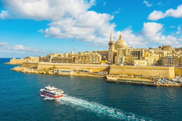 Aerial view of panorama Valletta city - capital of Malta country. Tourist red boat in Mediterranean sea. Blue sky