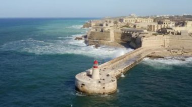 Ricasoli Kalesi 'ndeki kırmızı deniz fenerinin havadan görünüşü. Akdeniz 'de büyük dalgalar. Büyük liman. Malta ülkesi