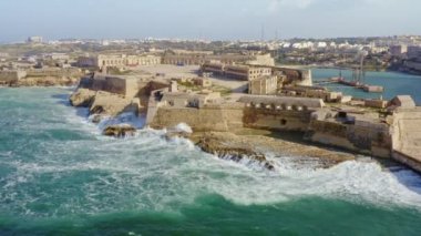 Ricasoli Kalesi 'ndeki kırmızı deniz fenerinin havadan görünüşü. Akdeniz 'de büyük dalgalar. Büyük liman. Malta adası