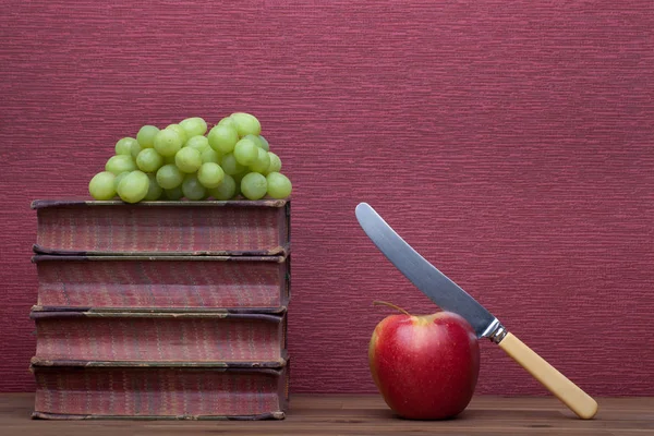Old books, apple with a knife and grapes — Stock Photo, Image