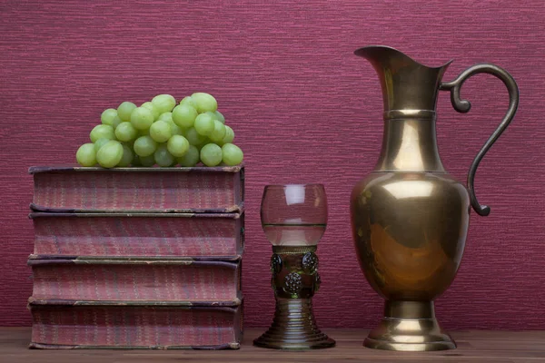 Renaissance, rummer wine glass, brass carafe, old books and grapes — Stock Photo, Image