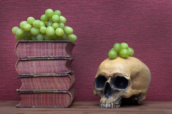 Old books, human skull and grapes