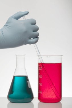 Laboratuvar eldivenlerindeki bir el kimyayı karıştırır. Laboratuvar şişelerinde sıvı. Bilimsel biyokimya laboratuvarı. Renkli sıvı.