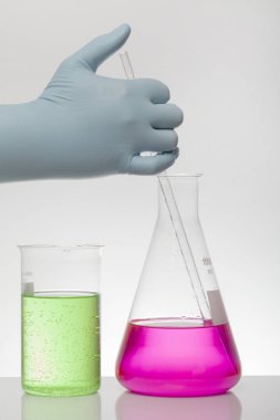 Laboratuvar eldivenlerindeki bir el kimyayı karıştırır. Laboratuvar şişelerinde sıvı. Bilimsel biyokimya laboratuvarı. Renkli sıvı.