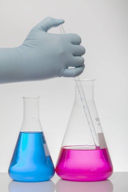 Laboratuvar eldivenlerindeki bir el kimyayı karıştırır. Laboratuvar şişelerinde sıvı. Bilimsel biyokimya laboratuvarı. Renkli sıvı.