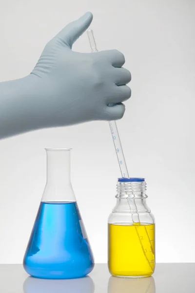 Uma mão em luvas de laboratório mistura a química. Líquido em garrafas de laboratório. Laboratório científico bioquímico. Líquido colorido . — Fotografia de Stock