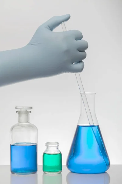 A hand in laboratory gloves mixes chemistry. Liquid in laboratory bottles. Scientific biochemical laboratory. Colorful liquid.