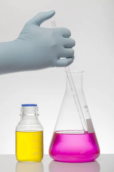 Рука в лабораторних рукавичках змішує хімію. Рідина в лабораторних пляшках. Наукова біохімічна лабораторія. Барвиста рідина . — стокове фото