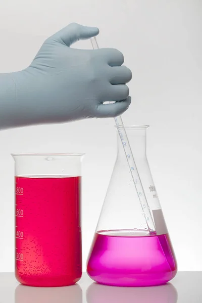 Egy kéz laboratóriumi kesztyűben összekeveri a kémiát. Folyadék laboratóriumi palackokban. Tudományos biokémiai laboratórium. Színes folyadék. — Stock Fotó