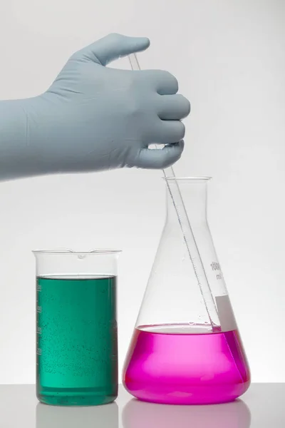 En hand i laboratoriehandskar blandar kemi. Vätska i laboratorieflaskor. Vetenskapligt biokemiskt laboratorium. Färgglad vätska. — Stockfoto