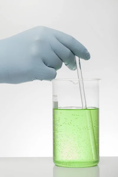 Une main dans les gants de laboratoire mélange la chimie. Liquide dans des bouteilles de laboratoire. Laboratoire biochimique scientifique. Liquide coloré . — Photo