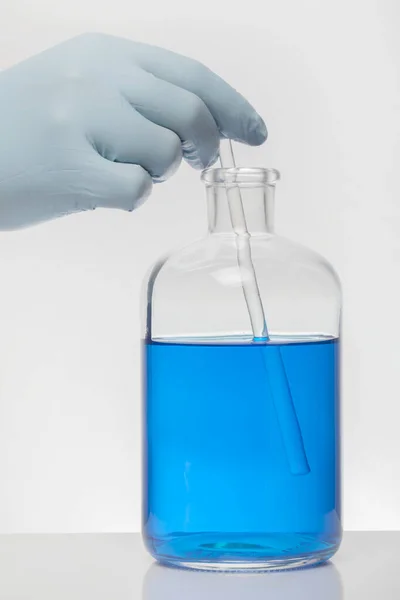 A hand in laboratory gloves mixes chemistry. Liquid in laboratory bottles. Scientific biochemical laboratory. Colorful liquid.
