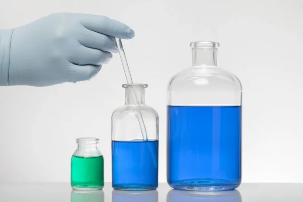 Laboratuvar eldivenlerindeki bir el kimyayı karıştırır. Laboratuvar şişelerinde sıvı. Bilimsel biyokimya laboratuvarı. Renkli sıvı. — Stok fotoğraf