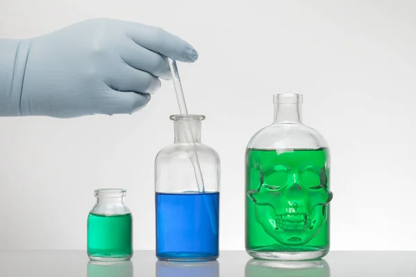 Egy kéz laboratóriumi kesztyűben összekeveri a kémiát. Folyadék laboratóriumi palackokban. Tudományos biokémiai laboratórium. Színes folyadék. — Stock Fotó