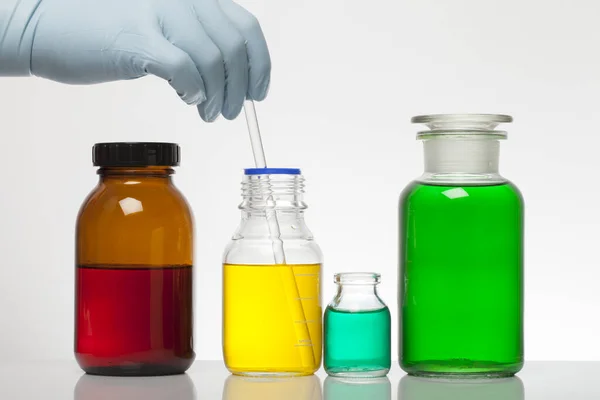 A hand in laboratory gloves mixes chemistry. Liquid in laboratory bottles. Scientific biochemical laboratory. Colorful liquid. — ストック写真