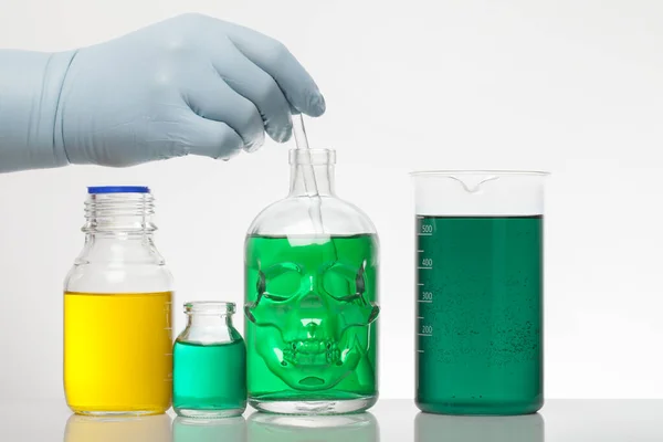 Une main dans les gants de laboratoire mélange la chimie. Liquide dans des bouteilles de laboratoire. Laboratoire biochimique scientifique. Liquide coloré . — Photo