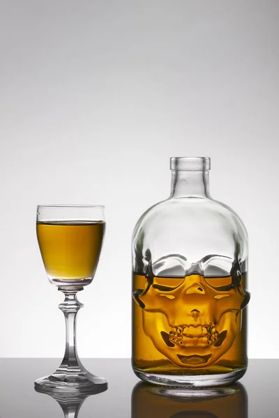 A skull bottle and crystal glasses with a liquid, alcohol drink.