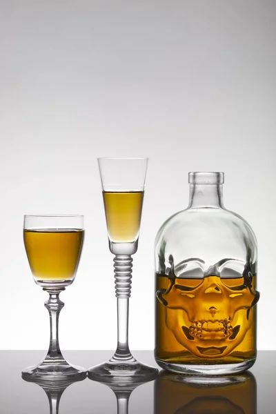 A skull bottle and crystal glasses with a liquid, alcohol drink.