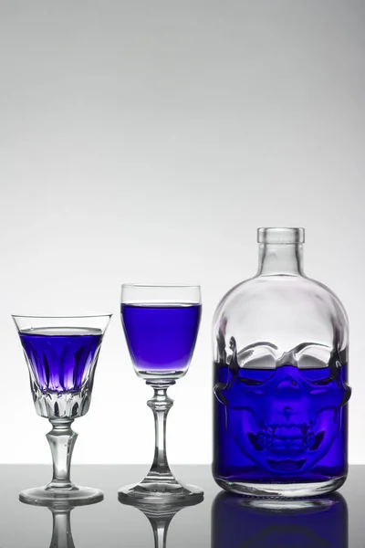 Una botella de cráneo y vasos de cristal con un líquido, bebida alcohólica . — Foto de Stock