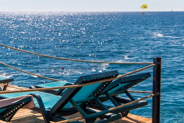 Vue sur la mer bleue, chaises longues sur la jetée, parapente jaune à l'horizon . Image En Vente