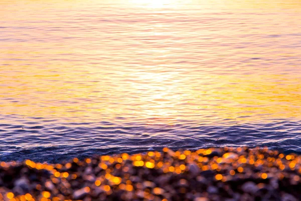 Golden pebbles on the seashore in the morning, at dawn, sea background
