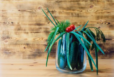 Taze sebzeler - domates, salatalık, yeşil soğan, dereotu, maydanoz - ahşap kahverengi arka planı olan cam bir vazoda.