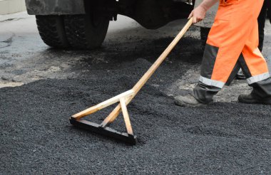 İşçi, asfalt karışımını ahşap bir paspasla düzleştiriyor.