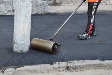 İşçi bir el silindiri ile asfalt yuvarlar