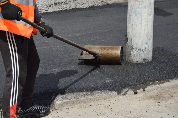 Worker rolls asphalt with a hand roller