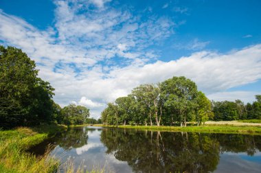 Güzel durgun göl ufukta ağaçlar ve gökte beyaz kabarık bulutlar. Kulübede huzurlu bir yaz günü. Göldeki büyük yeşil ağaçlar