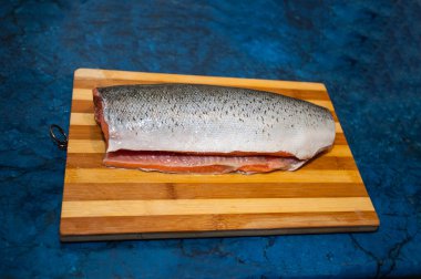 Tahta bir kesme tahtasındaki taze, çiğ, kırmızı bir balık parçası, siyah bir arka planda izole edilmiş. Ahşap kesim tahtasının üzerinde duran güzel somon filetosu, yemek pişirme ve sağlıklı beslenme konsepti. Mavi torba üzerinde