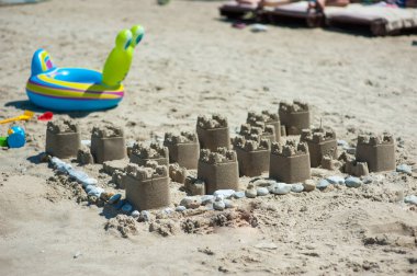 Kumlu bir sahilde kumdan bir kale, açık mavi bir yaz gökyüzüne karşı kurulmuş.