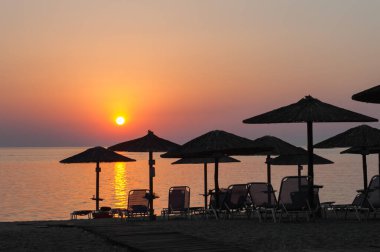 Gün batımında plaj şemsiyeleri, güneşli yataklar, plajda sıcak gün batımı.