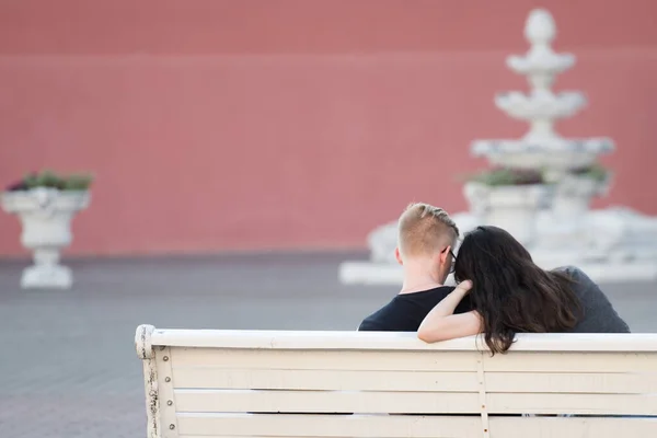 Pareja joven en un banco. fondo. Vista trasera de una pareja cariñosa sentada en un banco y mirando el teléfono —  Fotos de Stock