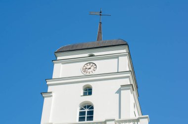 Mavi gökyüzüne karşı beyaz bir binanın tepesindeki saat.