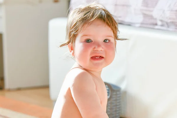 Het kind zit in de slaapkamer naast het bed. Een klein meisje zit op de vloer in de slaapkamer en speelt. Educatieve spelletjes voor kinderen. Lichte slaapkamer, tapijt bij het bed — Stockfoto