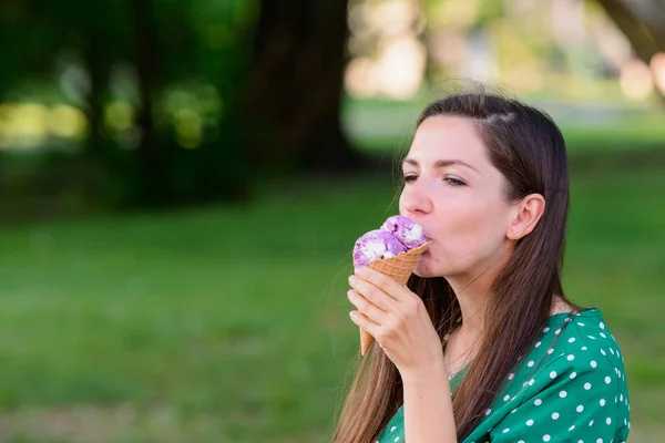 緑の背景でアイスクリームを食べる女の子碑文の場所だ緑の背景にアイスクリームを持つ若い都会の女性の肖像画。白い水玉のついた緑色のドレスでアイスクリームを食べる女の子 — ストック写真