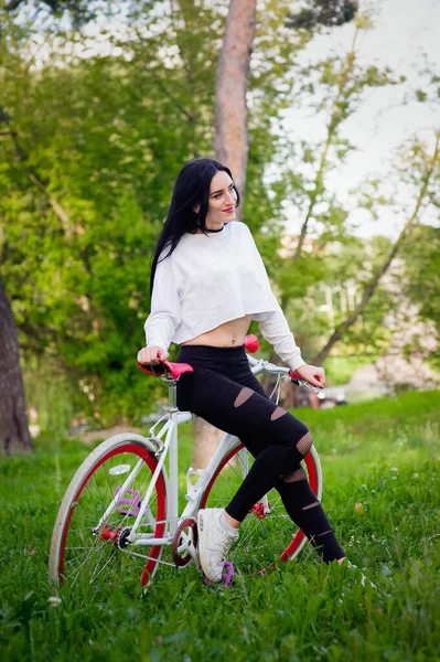 Hermosa chica posando en una bicicleta. bicicleta blanca y roja. caminar en la naturaleza. estilo de vida saludable. fin de semana en la naturaleza Retrato de una hermosa chica feliz en una camiseta blanca. lugar para escribir — Foto de Stock